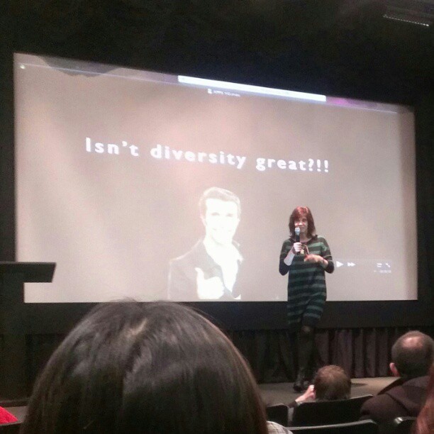 Nancy talking on microphone in front of a slide projection saying "Isn't diversity great?!!”